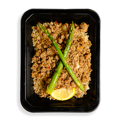 a container if filled with ground turkey over rice and two stalks of asparagus and a lemon wedge sit atop this delicious mixture of food. the togo meal container indicates that this is a health prepared meal designed for someone loosing weight or bulking up.