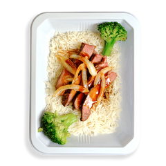 Thinly sliced flank steak over white rice, drizzled with low-sodium teriyaki sauce, is neatly arranged in a white to-go container. Bright green broccoli and julienned onions add a fresh, vibrant touch to this thoughtfully prepared meal—ideal for those who value healthy eating without compromising on flavor or quality.
